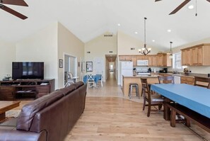 A spacious living room with a brown leather couch, a television, and a dining area with a blue tablecloth.