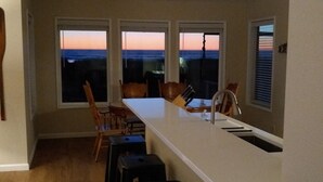 Eine moderne Küche mit einer zentralen Kochinsel, drei Fenstern und Blick auf den Sonnenuntergang.