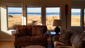 Ein Wohnzimmer mit zwei Sofas, die zu einem großen Fenster mit Blick auf einen Strand ausgerichtet sind.