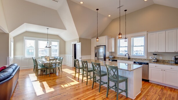 A spacious kitchen with a central island, white cabinetry, and a dining area with a table and chairs. - 5547- Sailfish Station - Nags Head Luxury Home Private Pool OBX (Nags Head)