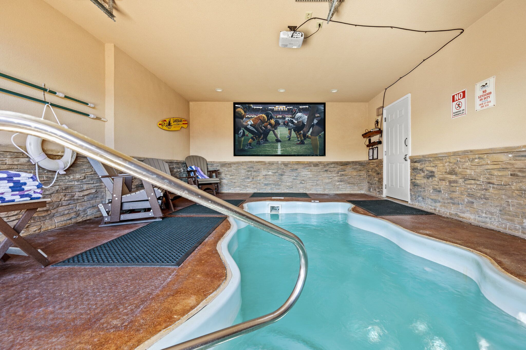An indoor swimming pool with a stone wall backdrop, a projector screen, and a lifebuoy.