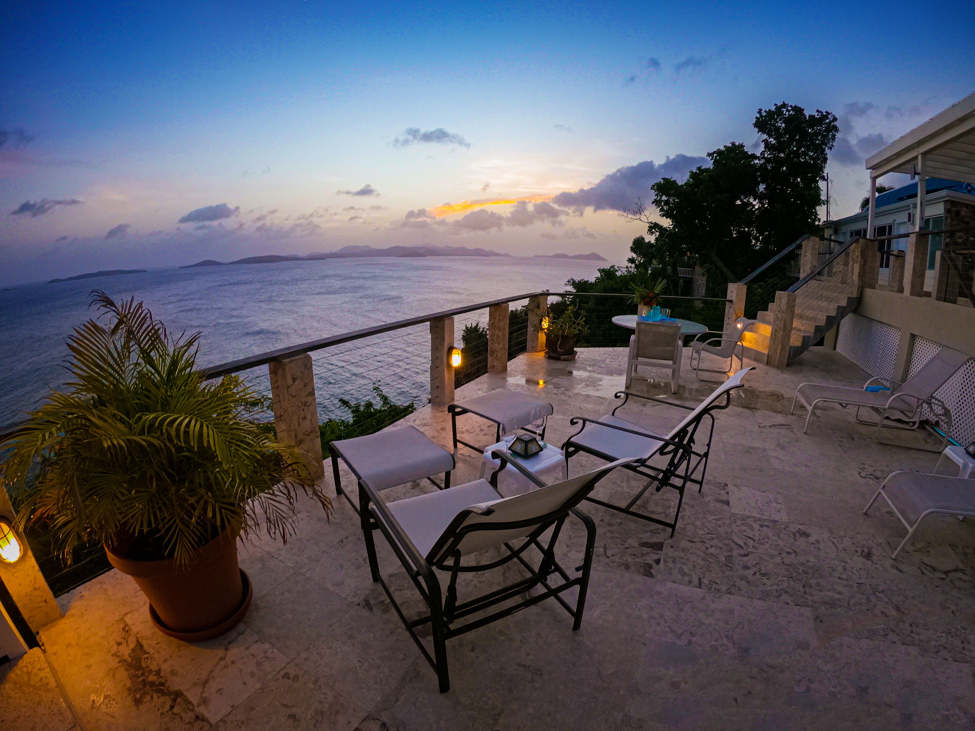 A terrace with outdoor furniture, a potted plant, and a view of the sea at dusk.