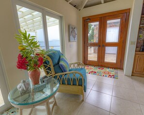 A room with a glass table, wicker chair, and a potted plant.