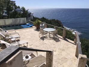 A terrace with a pool, lounge chairs, and a table, overlooking a coastal view.