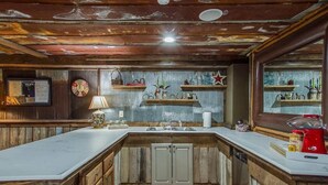Una cocina rústica con armarios de madera, un lavabo y una encimera. Hay estantes con objetos decorativos y un reloj en la pared.