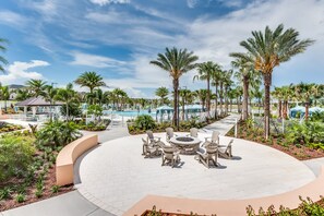 Un espace aménagé au bord de la piscine, avec des sièges disposés en cercle, des palmiers et un ciel d’un bleu limpide.