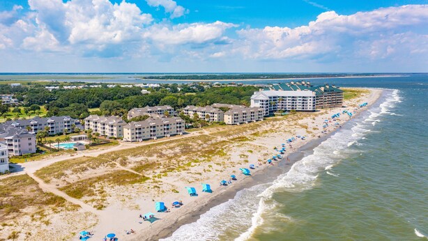 A coastal hotel with multiple buildings, a beach with umbrellas, and a view of the ocean. - Direct Oceanfront w/ Views! Pool Access, screened porch - 202B Port O Call (Isle of Palms)