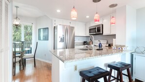 A modern kitchen with white cabinets, stainless steel appliances, and a granite countertop. - Direct Oceanfront w/ Views! Pool Access, screened porch - 202B Port O Call (Isle of Palms)