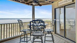 A covered outdoor seating area with a view of the beach, featuring a table and chairs, a ceiling fan, and a sign reading "ISLE OF PALMS". - Direct Oceanfront w/ Views! Pool Access, screened porch - 202B Port O Call (Isle of Palms)