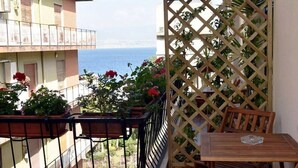 Un balcon avec vue sur la mer, des plantes en pot et une table en bois.