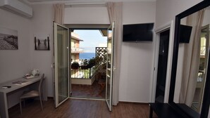 Une chambre dotée d’un bureau, d’une chaise, d’une télévision et d’un balcon offrant une vue sur la mer.