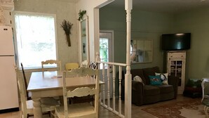 Un coin repas avec une table et des chaises blanches, un coin cuisine avec un réfrigérateur, et un salon avec un canapé et un téléviseur.