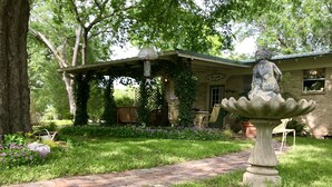 Un jardin avec une fontaine en pierre, un chemin en briques et une maison sur laquelle est accrochée une pancarte « Bienvenue ».