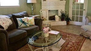 Un salon avec une cheminée, un canapé, une table basse en verre et une porte donnant sur une autre pièce.