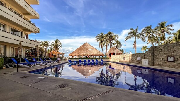 A pool area with blue lounge chairs, a thatched-roof structure, and palm trees. - Beautiful Ground Floor 2 BR Suite at Ixchel (Isla Mujeres)