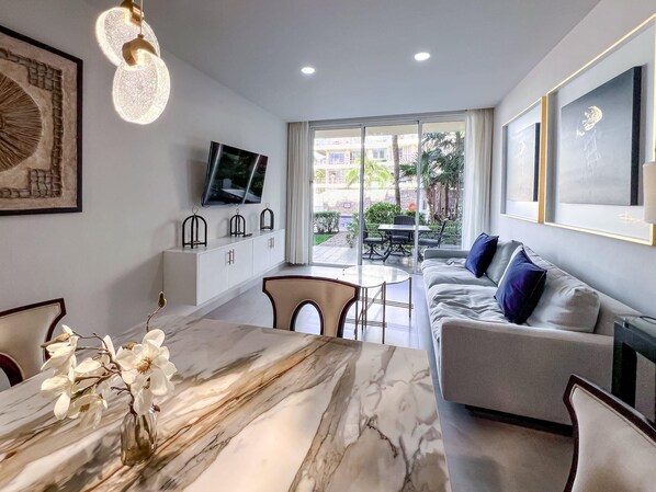 A modern living room with a marble dining table, a sofa, and a TV mounted on the wall.