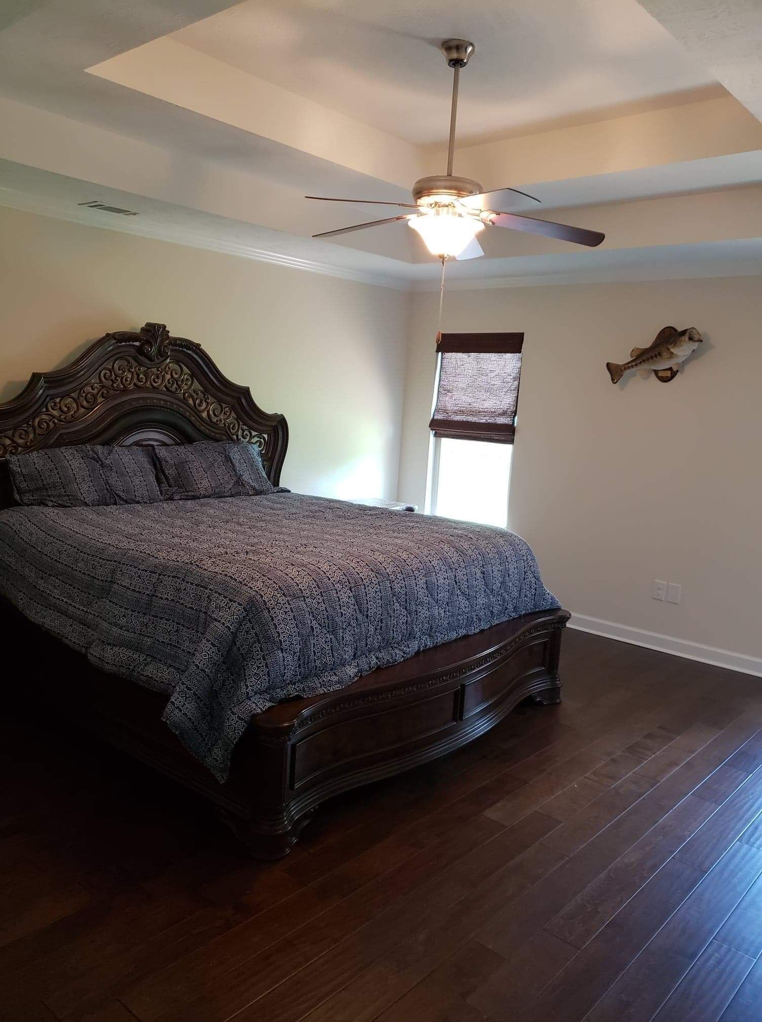 Une chambre avec un lit en bois, un ventilateur de plafond et une fenêtre avec des stores.
