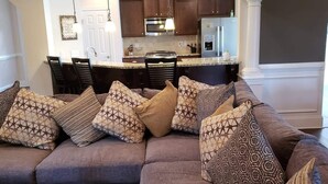 En moderne stue med en hjørnesofa, spiseområde og køkken i baggrunden.