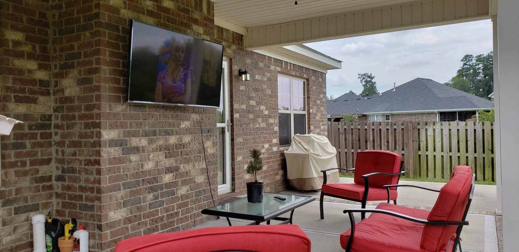 A covered patio area with brick walls, a television mounted on the wall, and red outdoor furniture.