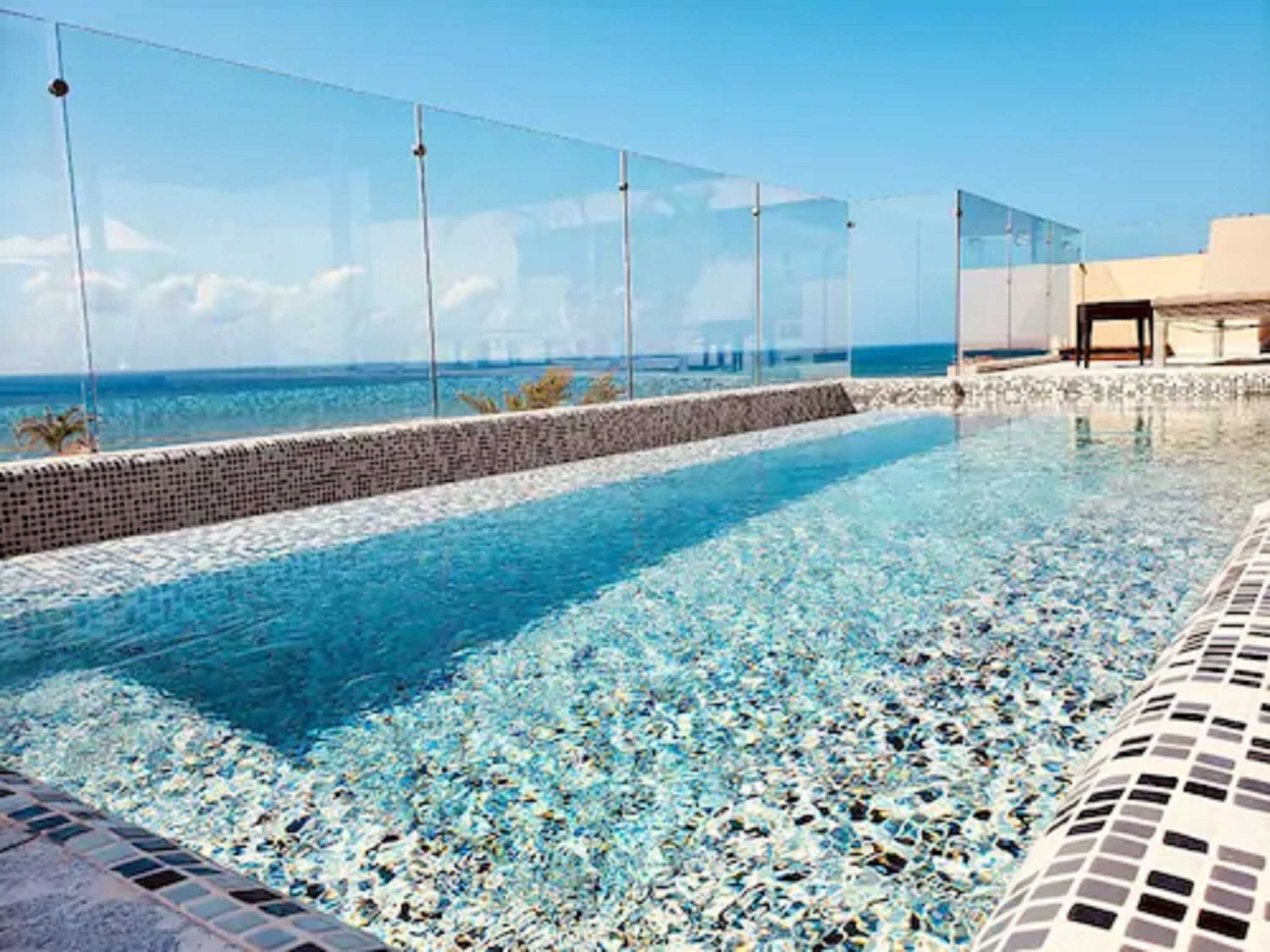 A clear blue infinity pool with a pebble bottom, surrounded by a glass barrier and a stone wall.