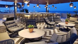 An outdoor seating area with round tables and chairs, a bar, and a view of the sea. - Singular Joy Downtown Residences (Playa del Carmen)