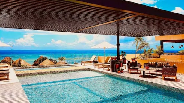 A pool area with lounge chairs and umbrellas, overlooking a beach with clear blue water and a view of the ocean. - Singular Joy Downtown Residences (Playa del Carmen)