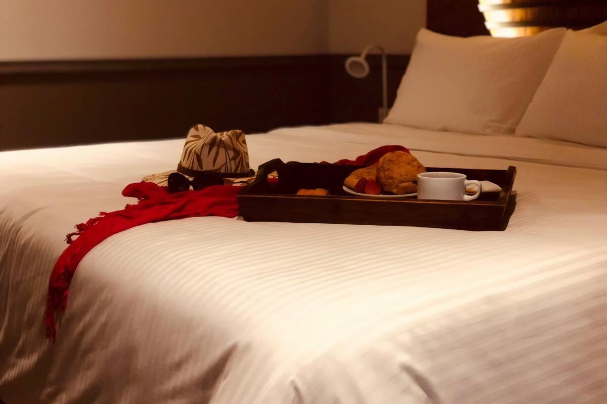 A neatly made bed with a tray of breakfast items including croissants, a cup of coffee, and a red scarf.
