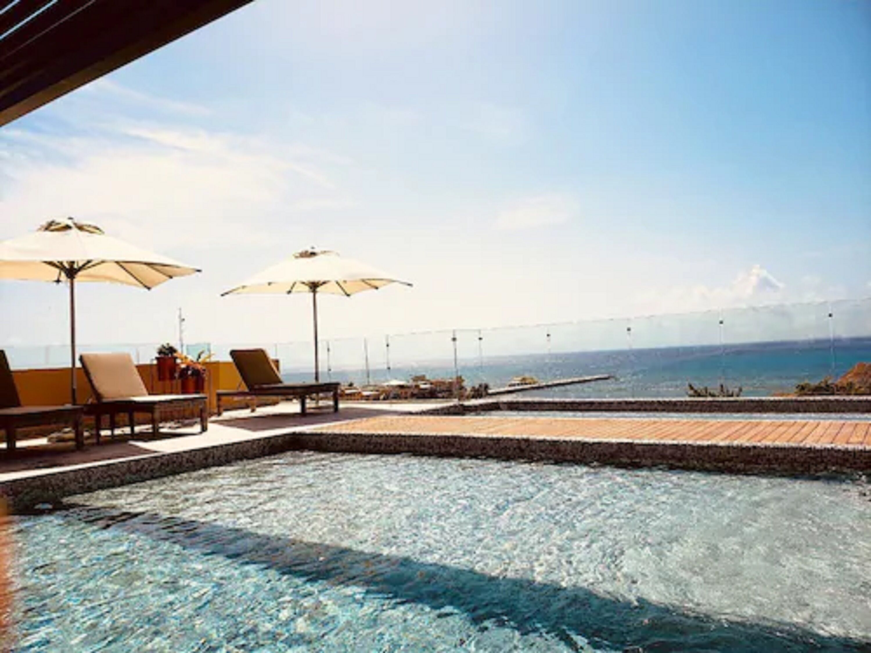Uma piscina infinita com espreguiçadeiras e guarda-sóis, com vista para um corpo de água e uma ponte ao longe.