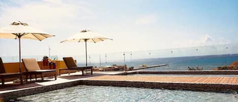 Una piscina infinita con sillones de descanso y sombrillas, con vista a un cuerpo de agua y un puente distante.