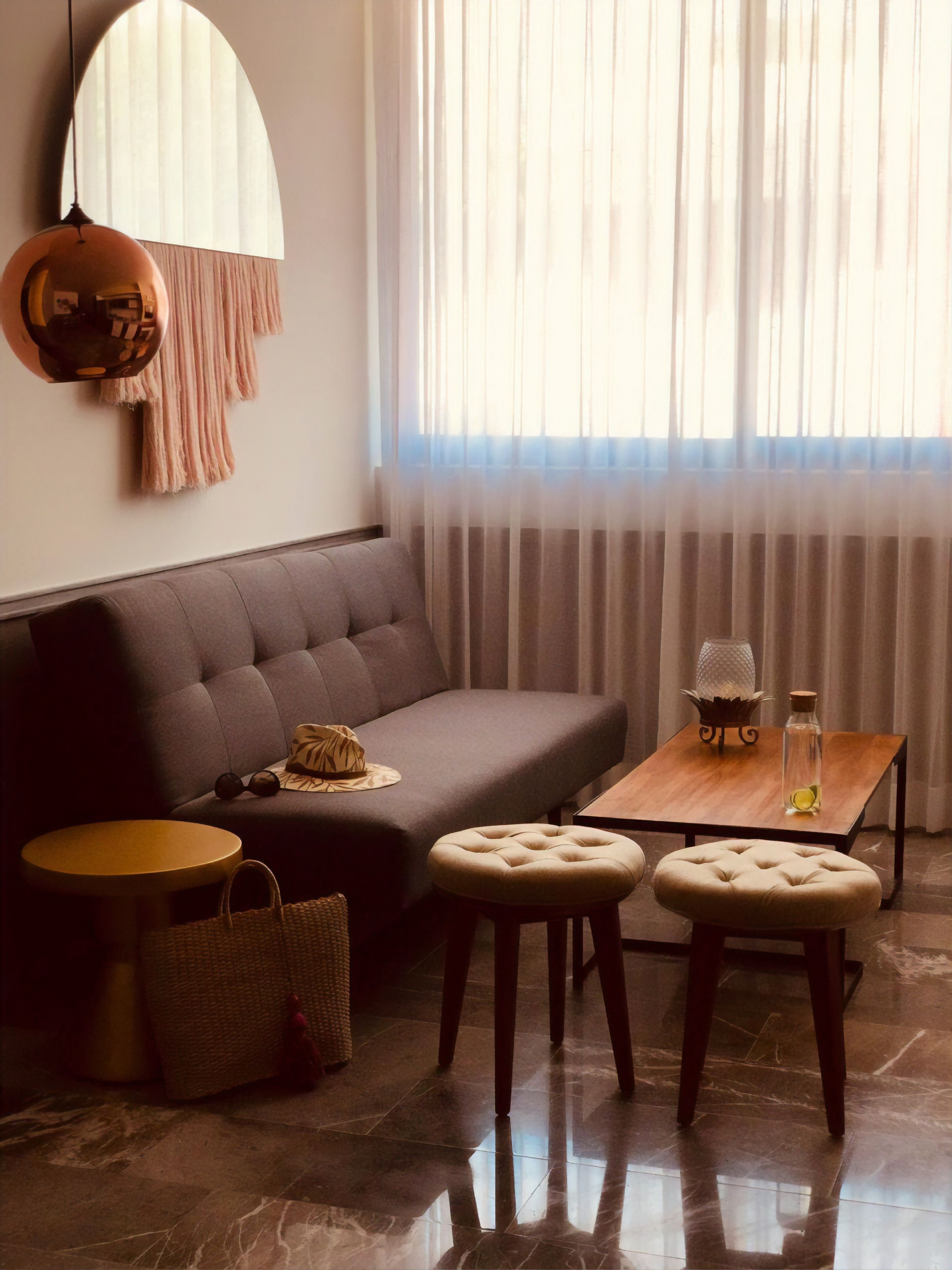 A modern living room with a grey sofa, two ottomans, a wooden coffee table, and a hanging lamp.