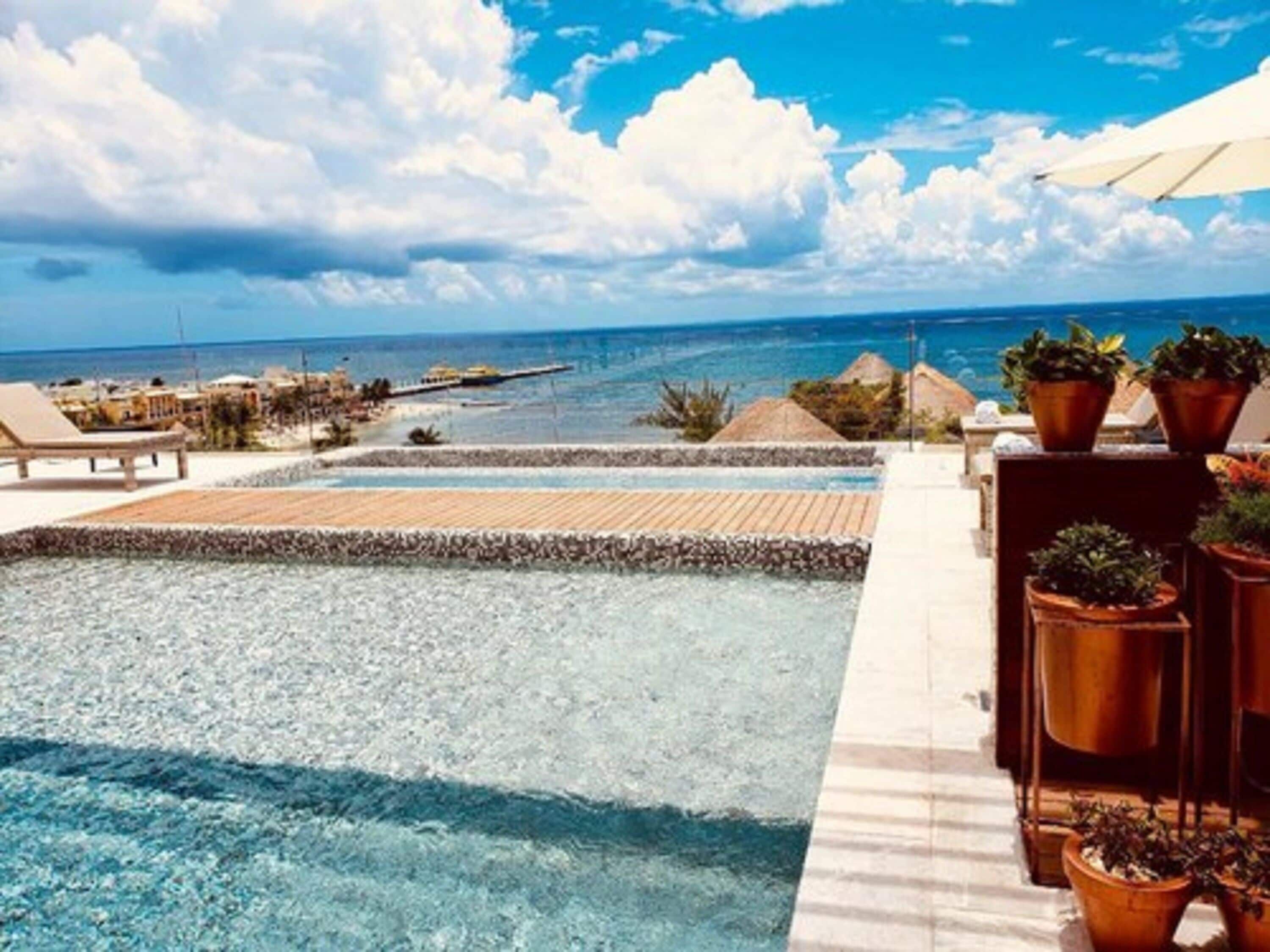 A poolside view with clear water, lounge chairs, and potted plants.