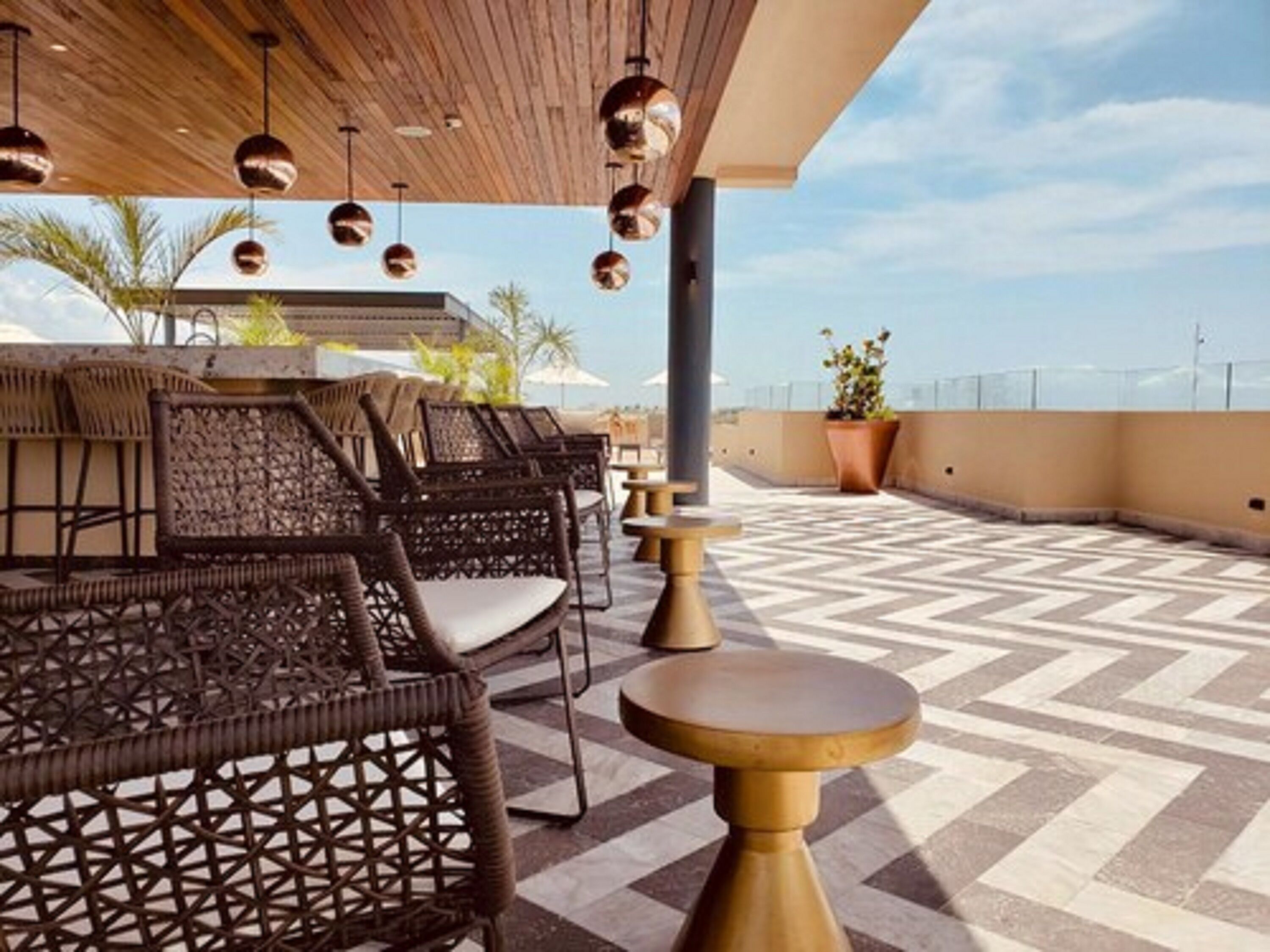 A rooftop terrace with wicker furniture, a patterned floor, and hanging pendant lights.