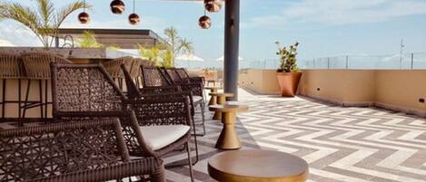 A rooftop terrace with wicker furniture, a patterned floor, and hanging pendant lights.