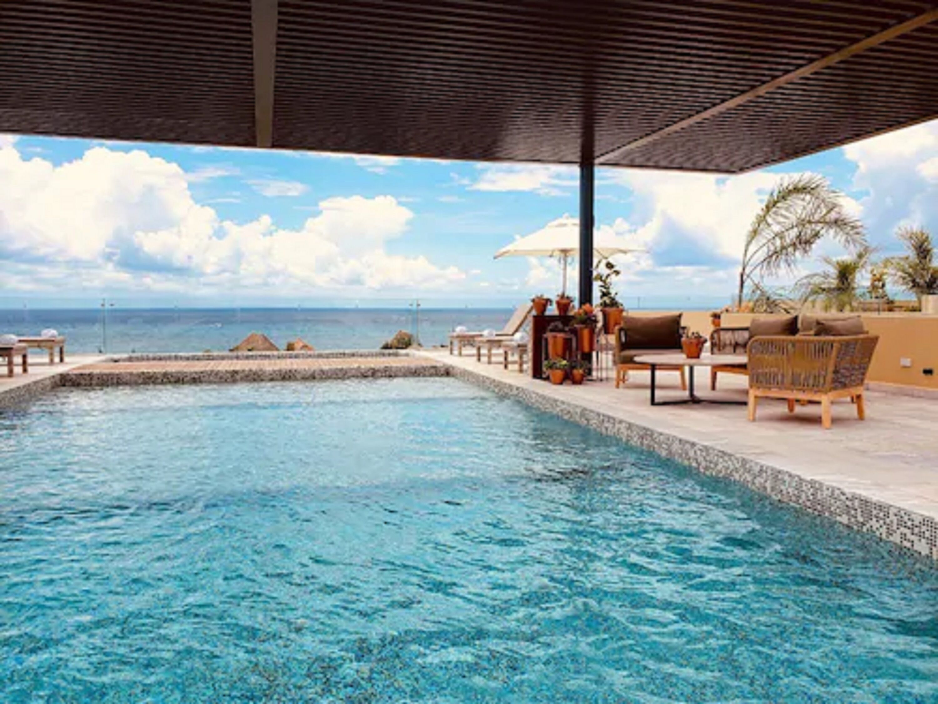 Ein Poolbereich mit Liegestühlen und Sonnenschirmen mit Blick auf einen Strand und das Meer.