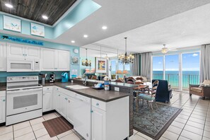 Una cocina moderna con armarios blancos, una isla central y un ventanal con vistas al océano.