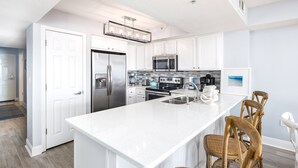 A modern kitchen with white cabinetry, stainless steel appliances, and a large island with bar stools. - Sea Dunes 202 • Amazing Ocean View, Private Balcony, Pool, Free Hot Tub, Beach Service (Fort Walton Beach)