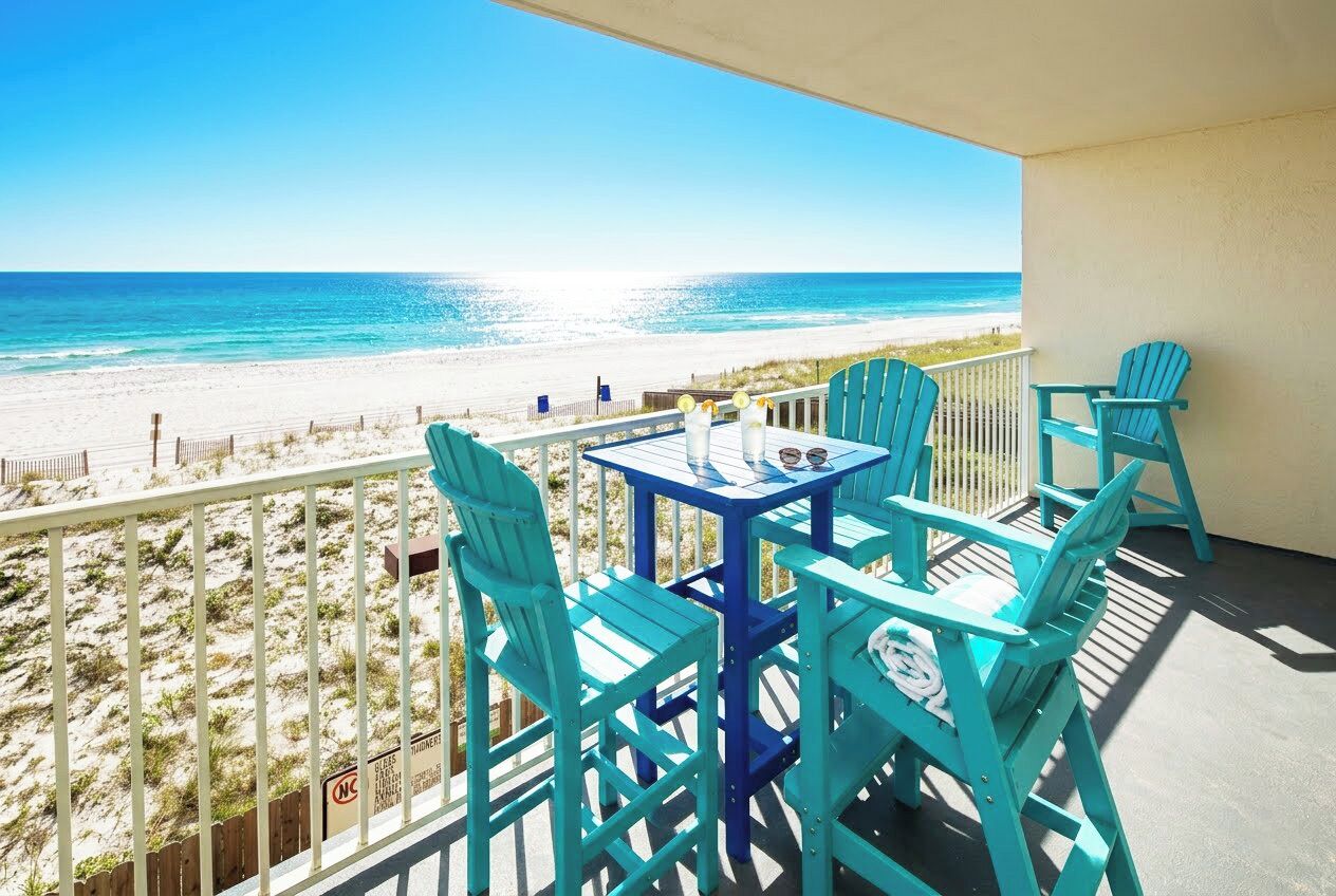 Un balcon donnant sur une plage, avec des chaises et une table de couleur turquoise.