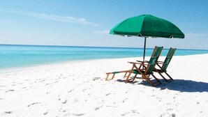 A beach scene with a green umbrella and two wooden beach chairs on a sandy shore. - Sea Dunes 202 • Amazing Ocean View, Private Balcony, Pool, Free Hot Tub, Beach Service (Fort Walton Beach)