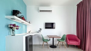 A compact living space with a kitchenette, a dining area with two chairs, a TV mounted on the wall, and a large window with curtains. - Just steps from downtown with balcony (Isla Mujeres)