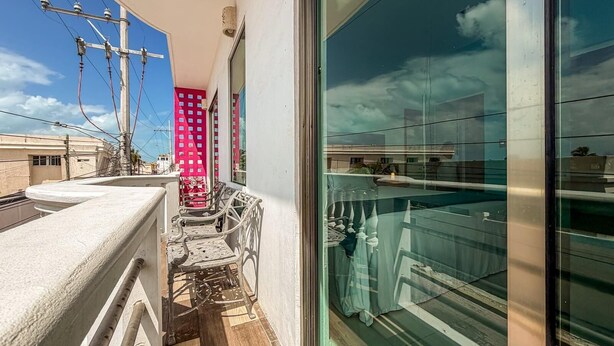 A balcony with a white balustrade, a red patterned wall, and a glass door leading to a balcony with a view of the sky and clouds. - Just steps from downtown with balcony (Isla Mujeres)