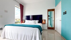 A modern bedroom with a large bed, a nightstand, a mirror, and a view of the outdoors. - Just steps from downtown with balcony (Isla Mujeres)