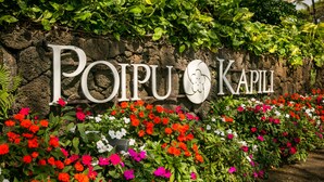 Ein Schild mit dem Namen "Poipu Kapili", umgeben von bunten Blumen.