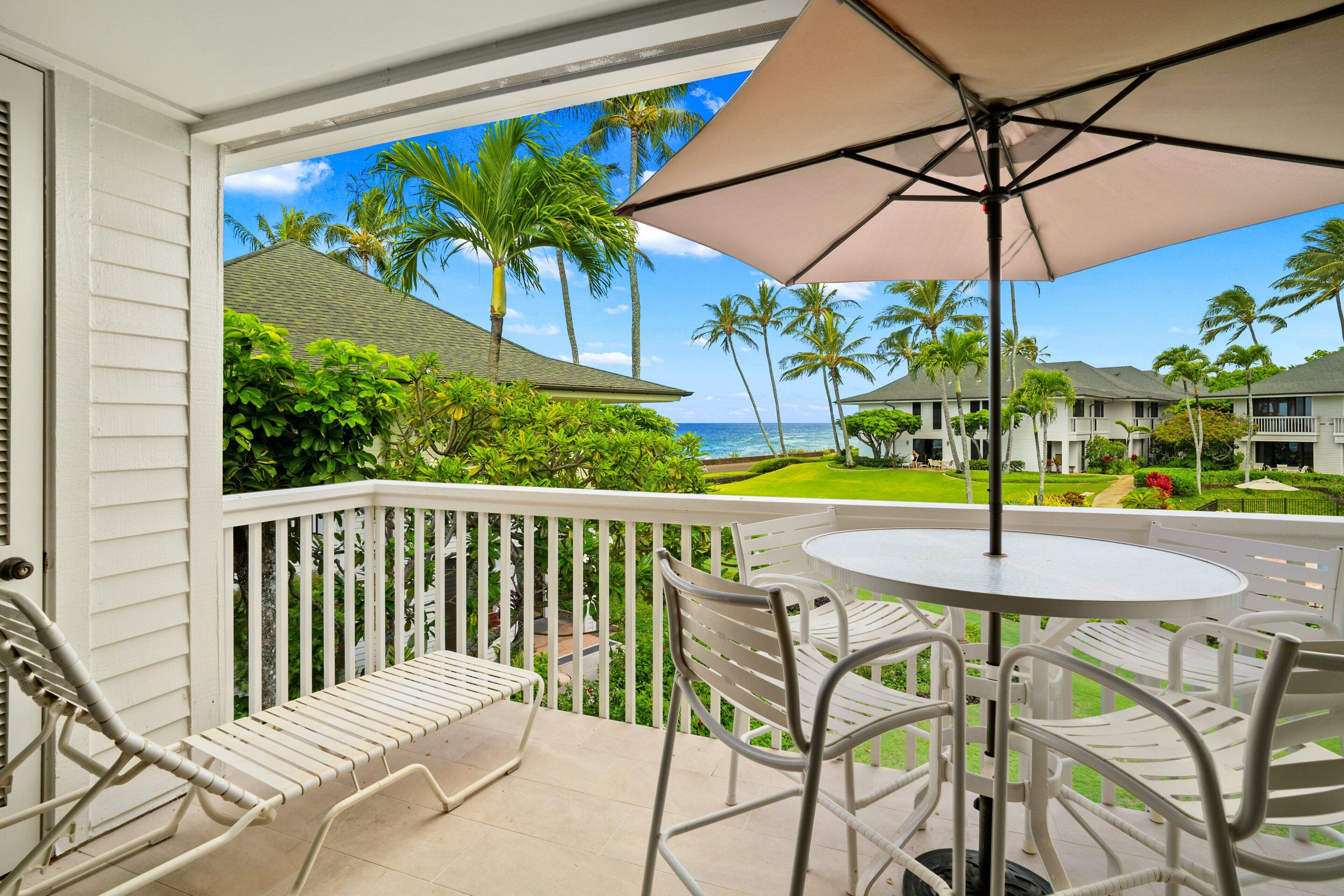 Un balcon avec une balustrade blanche, une table ronde entourée de chaises et un grand parasol.