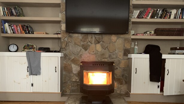 A living room with a stone fireplace, a flat-screen TV mounted above it, and wooden cabinets on either side.