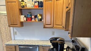 A compact kitchen with wooden cabinets, a dishwasher, a coffee maker, and a granite countertop.