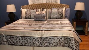 A bedroom with a bed, two nightstands, a window with white curtains, and wooden flooring.