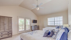 Une chambre spacieuse avec un grand lit, un ventilateur de plafond, une télévision et une fenêtre équipée de stores.