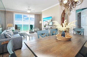 A living room with a wooden dining table, blue chairs, a sofa, and a TV.