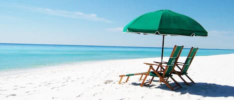 En strandscen med ett grönt parasoll och två trästolar på en sandstrand.