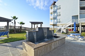 Un patio con fuente de agua, mesas de picnic y un edificio con balcones.
